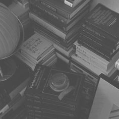 a pile of books sitting on top of a table next to a lamp and book case