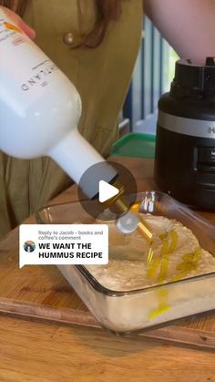 a woman pouring batter into a glass dish on top of a wooden table next to a blender