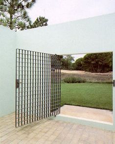 an open door in the middle of a brick floored area with grass and trees