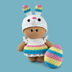 a crocheted stuffed animal wearing a colorful dress and hat with an egg on the ground