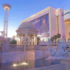 a fountain in front of a large building with lights on it's sides and palm trees