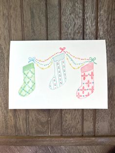 a card with two stockings hanging from it's side on a wooden wall next to a piece of wood