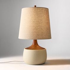 a table lamp with a beige shade on it and a white base is shown in front of a gray background