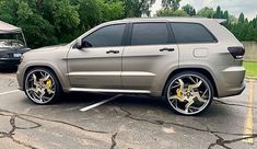 a silver jeep parked in a parking lot next to another car with yellow rims