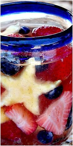 a glass jar filled with fruit on top of a stone counter topped with berries and blueberries