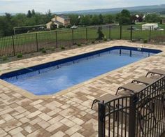 an above ground swimming pool surrounded by brick pavers and fenced in lawn area