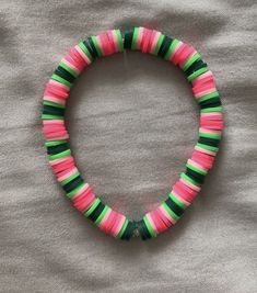 a pink, green and black beaded bracelet on top of a white cloth covered bed