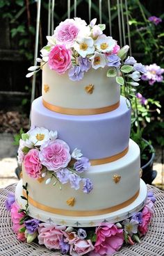 a three tiered cake with flowers on the top and bottom is sitting on a wicker table