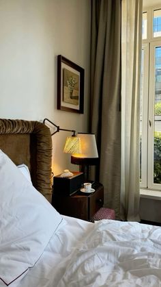 a bed sitting next to a window with white sheets and pillows on top of it