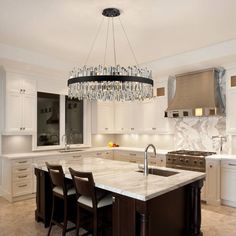 a chandelier hanging from the ceiling in a kitchen with white cabinets and marble counter tops