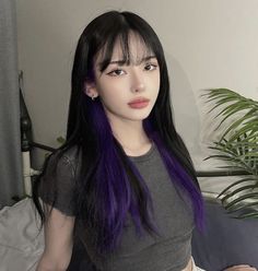 a woman with purple hair is sitting on a bed and looking at the camera while wearing a gray shirt