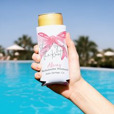 a person holding up a can of beer near a swimming pool