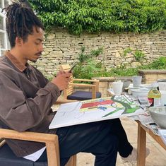 a man with dreadlocks sitting at a table painting