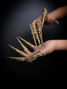 two hands are holding gold colored nails