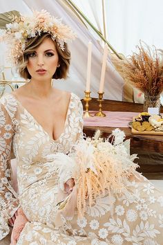 a woman in a wedding dress with flowers on her head sitting next to a cake