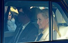 a woman sitting in the back seat of a car next to a man wearing a suit and tie