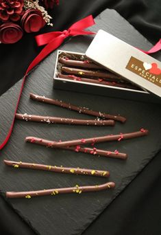 chocolate sticks with sprinkles in a box on a black surface next to red ribbon