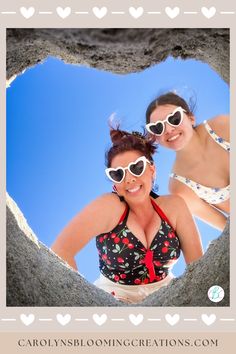 two women in bikinis are seen through a hole in the sand with heart shaped sunglasses