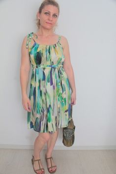 a woman standing in front of a white wall wearing sandals and a dress with colorful print