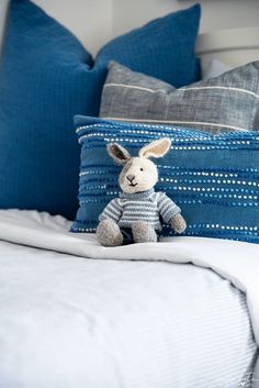 a stuffed animal sitting on top of a bed next to blue pillows and pillow cases