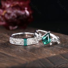 two silver rings with green stones on top of a wooden table next to a red flower