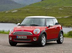 a small red car parked on the side of a road next to a body of water