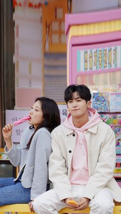 two people sitting on a bench in front of a candy store with one person brushing their teeth