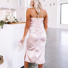 a woman standing in front of a counter wearing a pink slip on dress and heels