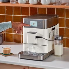 a woman is pressing the button on a coffee machine with milk in front of her