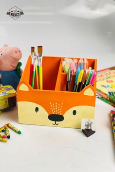 an orange box with pens and pencils in it on a table next to other items