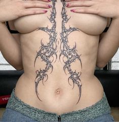 a woman with tattoos on her stomach holding her hands behind her back and looking at the camera