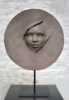 a sculpture of a woman's head on a black stand with a white wall in the background