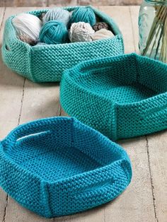 two knitted baskets sitting on the floor next to each other, one blue and one green