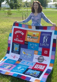 a woman standing in the grass holding up a colorful quilt that has been made into a blanket