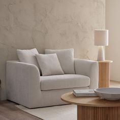 a white couch sitting next to a table on top of a wooden floor under a lamp