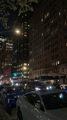 many cars are parked on the side of the road in front of tall buildings at night