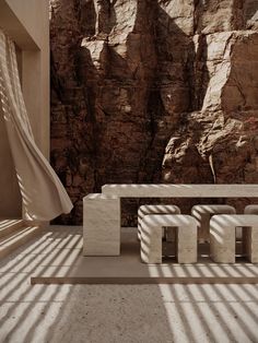 a table and benches are in front of a rocky mountain backdrop with long shadows on the floor