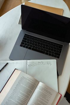 an open laptop computer sitting on top of a table next to a notebook and pen