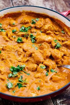 a red pot filled with chicken curry on top of a wooden table