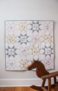 a wooden rocking horse next to a white wall with a quilt on it's back