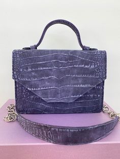 Meet the elegant and modern 'Daphne' top-handle bag crafted with the following characteristics: - Handcrafted - Snap-fastening front flap - Additional removable leather and chain shoulder strap for ease of carry - Croc-embossed bovine nubuck Italian leather - Fully lined with the brand΄s distinctive silk lavender lining - Discreet metal embossed label tag inside - Comes with dust bag It is big enough to fit your daily essentials and features interior slip pocket to keep your cards and keys secur Top Handle Satchel With Magnetic Closure, Luxury Purple Evening Satchel, Blue Formal Bag With Adjustable Handle, Blue Formal Bags With Adjustable Handle, Formal Blue Bag With Adjustable Handle, Luxury Evening Bag With Adjustable Strap And Double Handle, Elegant Purple Top Handle Satchel, Luxury Evening Bag With Adjustable Double Handle, Top Handle Evening Bag With Adjustable Strap