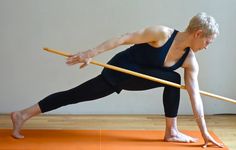 a woman is doing yoga with a pole in her hand and holding onto the floor