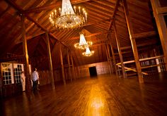 two people standing in a large room with chandeliers hanging from the ceiling and wooden floors