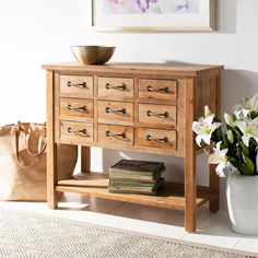 a vase with flowers and books is next to a wooden dresser in a white room