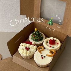 four cupcakes in a cardboard box decorated with christmas trees and other holiday treats