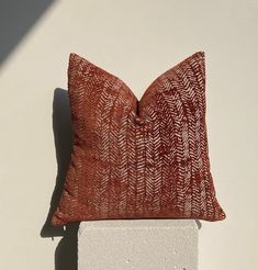 a red and white pillow sitting on top of a cement block next to a wall