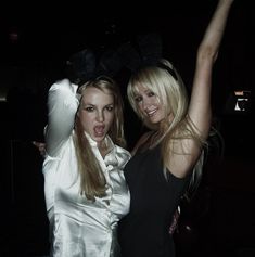 two beautiful young women standing next to each other in front of a dark background at a party