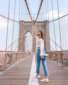 a woman standing on the side of a bridge with her hand in her pocket and looking at the camera