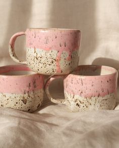 three pink and white coffee mugs sitting on top of each other in front of a white sheet