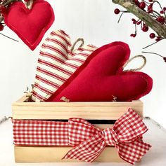 two red hearts in a wooden box with gingham ribbon on the bottom and a bow at the top